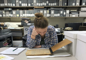 在满是档案资料的房间里，女孩俯身看着旧文件
