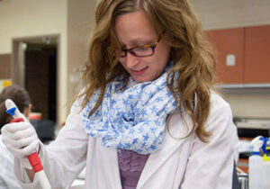 女孩穿着实验室工作服和围巾，在实验室使用吸液器