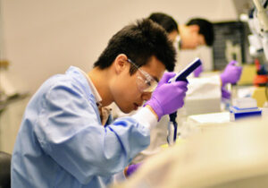 学生穿着实验室安全服，在实验室里吸液
