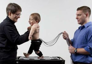 两名研究人员抱着一个装有电极的婴儿在跑步机上行走