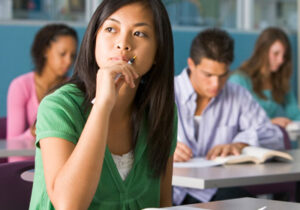 亚裔美国女学生坐在教室里，拿着笔思考