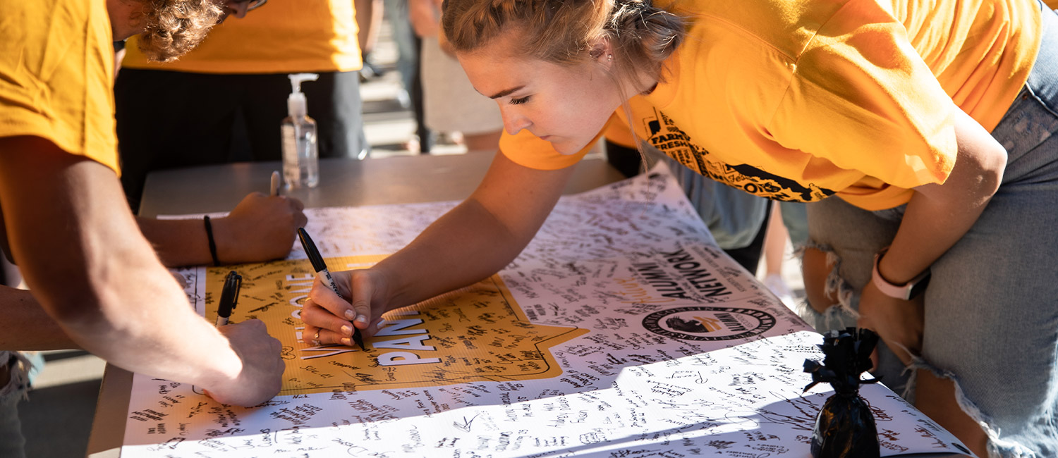 beplay客服有没有电话身着黄色t恤的威斯康辛大学学生在秋季欢迎标语上签名