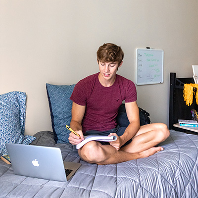 beplay客服有没有电话威斯康星大学白人男性学生坐在宿舍的床上学习